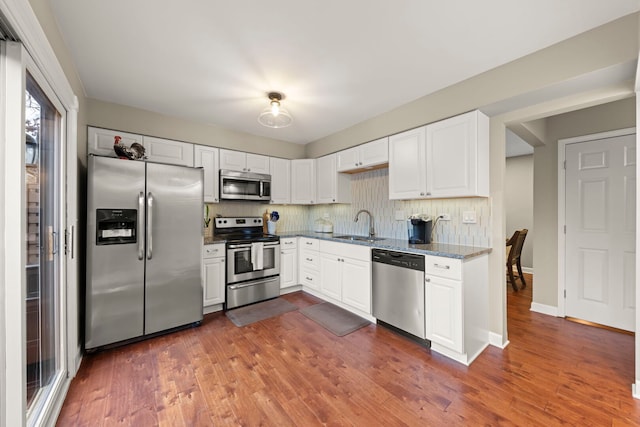 kitchen featuring dark wood-style flooring, decorative backsplash, appliances with stainless steel finishes, a sink, and dark stone counters