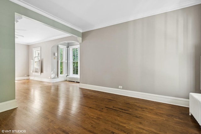 spare room with dark wood-style floors, arched walkways, radiator, and baseboards