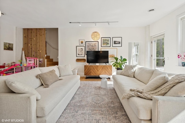 living area featuring stairway, rail lighting, and visible vents