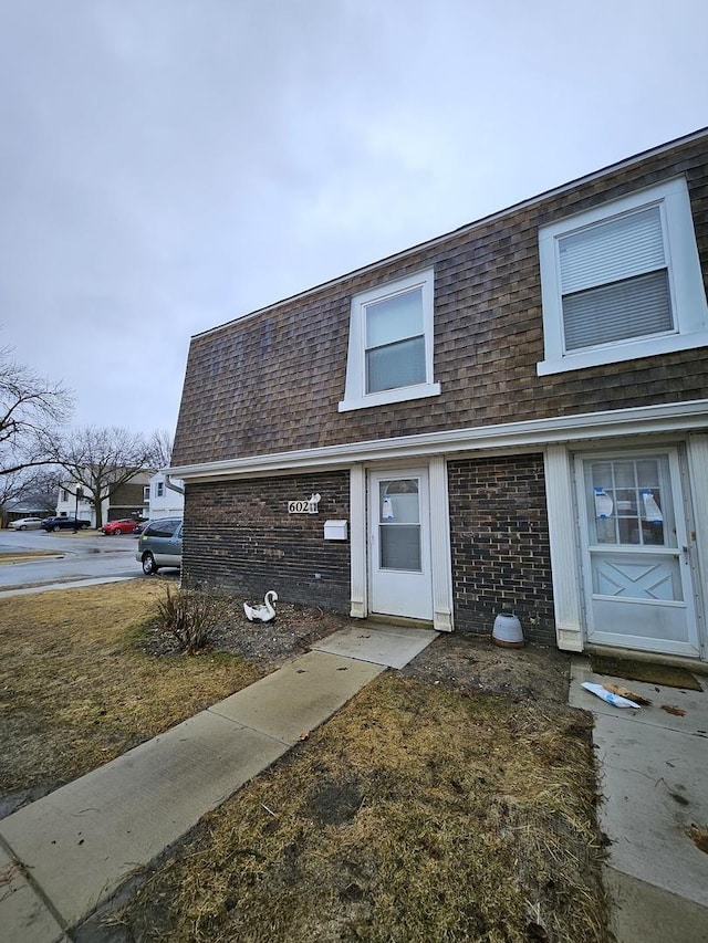 townhome / multi-family property with brick siding, mansard roof, and roof with shingles