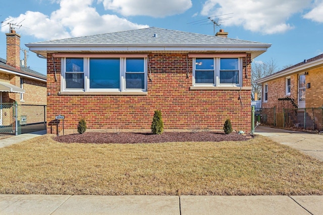 view of home's exterior featuring roof with shingles, brick siding, a lawn, and fence