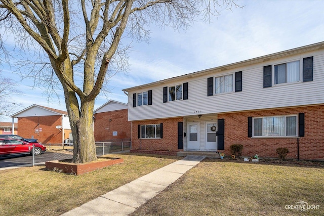 view of property with brick siding, a front lawn, and fence