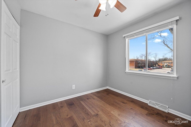 empty room with dark wood finished floors, visible vents, ceiling fan, and baseboards