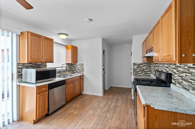 kitchen with a sink, range hood, stainless steel appliances, light wood finished floors, and light countertops