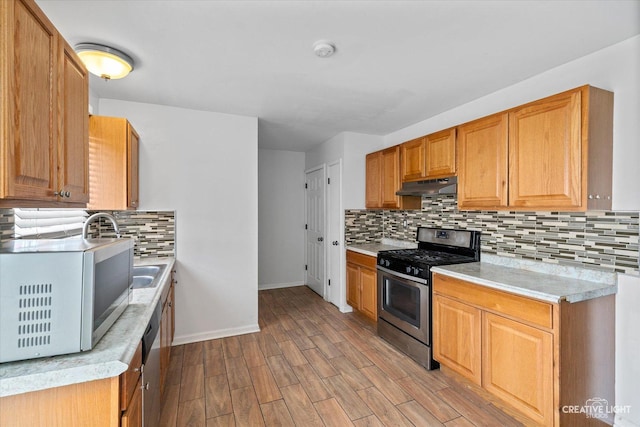 kitchen featuring stainless steel gas stove, under cabinet range hood, light wood-style floors, light countertops, and decorative backsplash