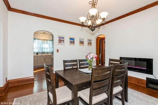 dining area featuring baseboards, arched walkways, wood finished floors, crown molding, and a chandelier