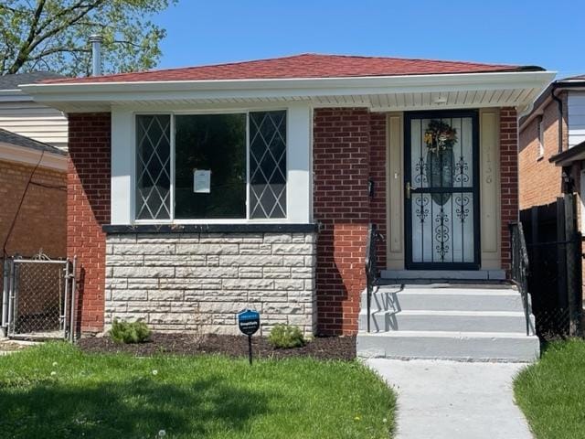 entrance to property featuring an attached garage, stone siding, a yard, and brick siding