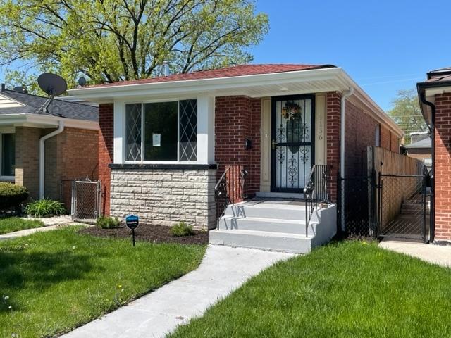 bungalow-style house featuring stone siding, a front lawn, fence, and brick siding