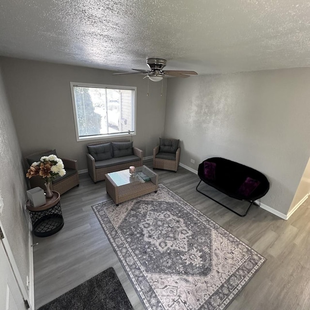 living room featuring a textured ceiling, wood finished floors, a ceiling fan, and baseboards
