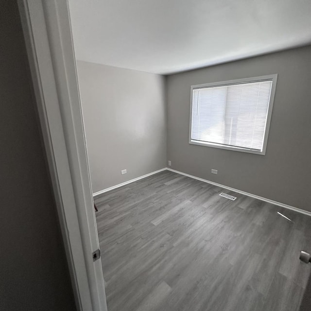spare room featuring dark wood-type flooring, visible vents, and baseboards