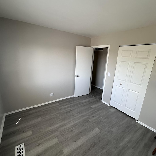 unfurnished bedroom featuring dark wood-style floors, baseboards, visible vents, and a closet