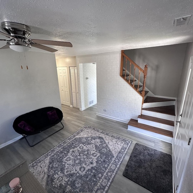 foyer featuring wood finished floors, brick wall, ceiling fan, baseboards, and visible vents