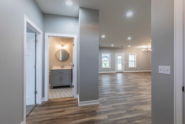 corridor with dark wood-style flooring, a notable chandelier, recessed lighting, a sink, and baseboards