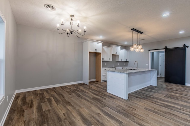 kitchen featuring a barn door, light stone counters, a sink, white cabinets, and an island with sink