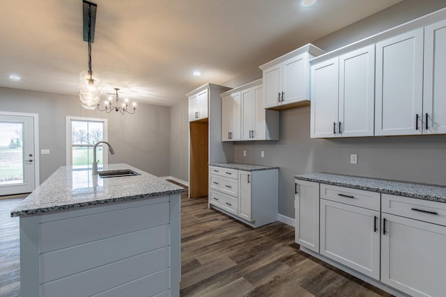 kitchen with an island with sink, a sink, decorative light fixtures, and white cabinets