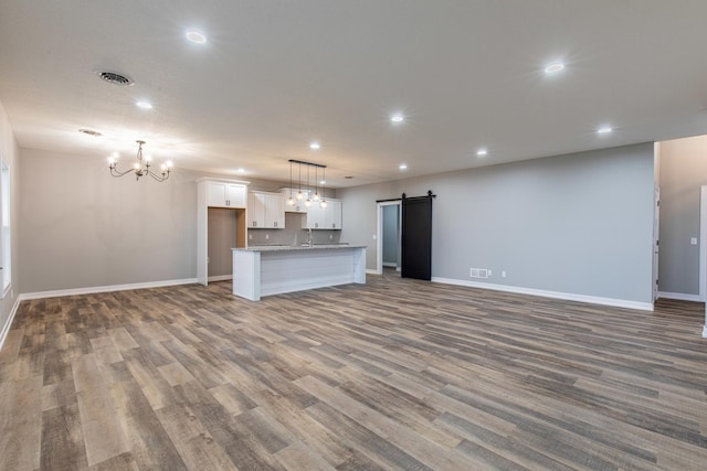 unfurnished living room with a barn door, recessed lighting, a notable chandelier, visible vents, and baseboards