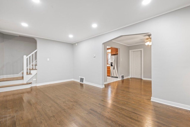 unfurnished living room with arched walkways, stairway, ornamental molding, wood finished floors, and baseboards