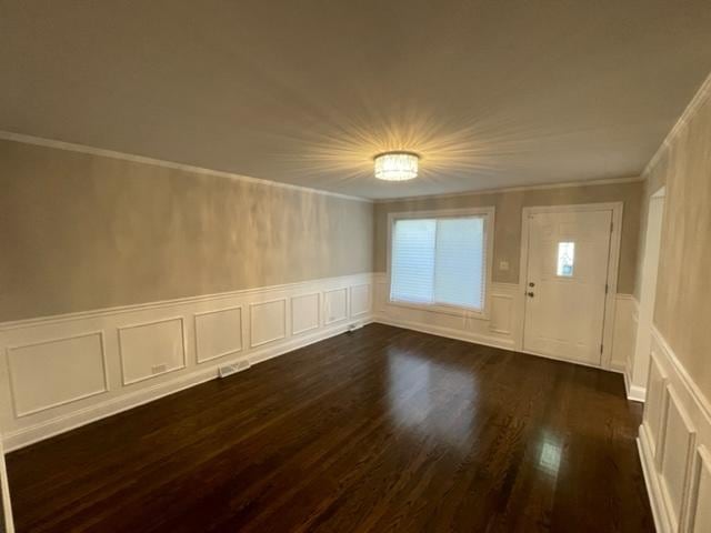 entrance foyer featuring a wainscoted wall, a decorative wall, dark wood-style flooring, and crown molding