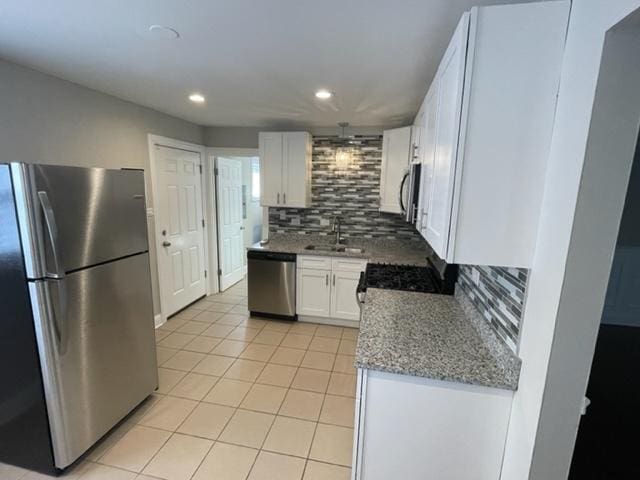 kitchen with light tile patterned floors, appliances with stainless steel finishes, light stone countertops, white cabinetry, and a sink