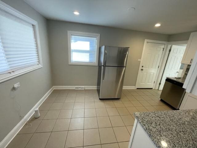 kitchen with light tile patterned floors, baseboards, light stone counters, freestanding refrigerator, and white cabinetry