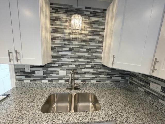 kitchen featuring light stone counters, white cabinets, a sink, and backsplash