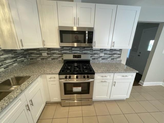 kitchen with tasteful backsplash, stainless steel appliances, light stone counters, and white cabinets