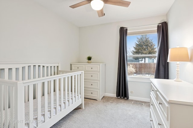 bedroom with ceiling fan, light colored carpet, visible vents, baseboards, and a nursery area