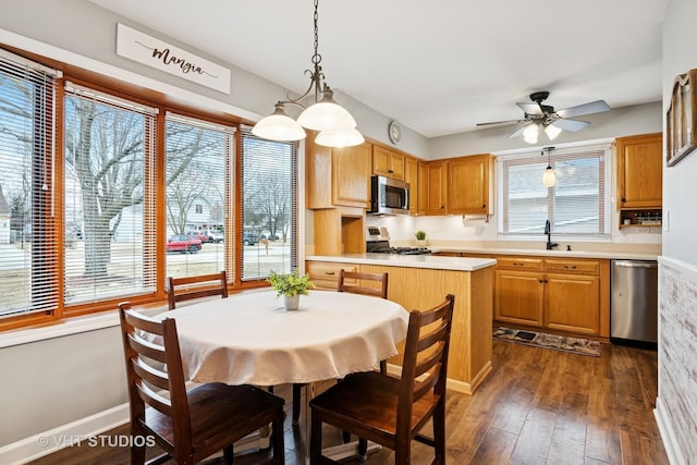 kitchen featuring stainless steel appliances, a sink, light countertops, dark wood-style floors, and decorative light fixtures