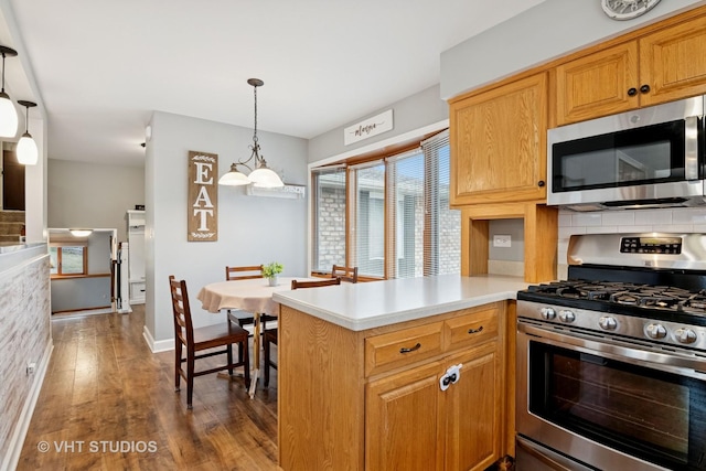 kitchen featuring a peninsula, dark wood-style flooring, light countertops, appliances with stainless steel finishes, and decorative light fixtures