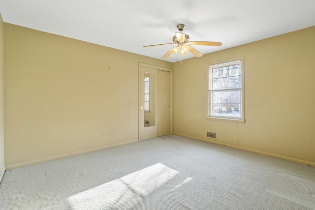 spare room featuring light carpet, a ceiling fan, and baseboards