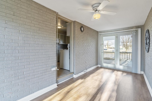 unfurnished room with a ceiling fan, brick wall, baseboards, and wood finished floors