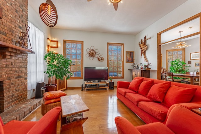 living room featuring light wood-type flooring, a fireplace, baseboards, and ceiling fan with notable chandelier