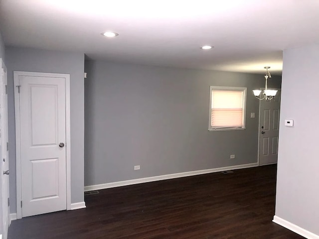 spare room featuring a chandelier, dark wood-style flooring, recessed lighting, and baseboards