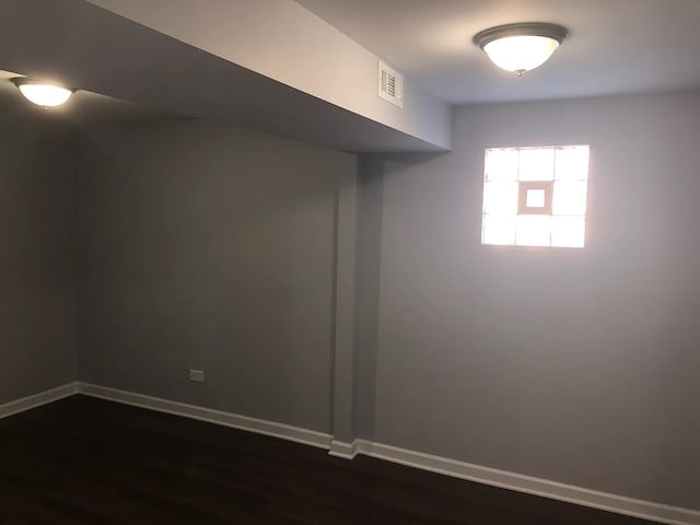 empty room featuring dark wood-style flooring, visible vents, and baseboards