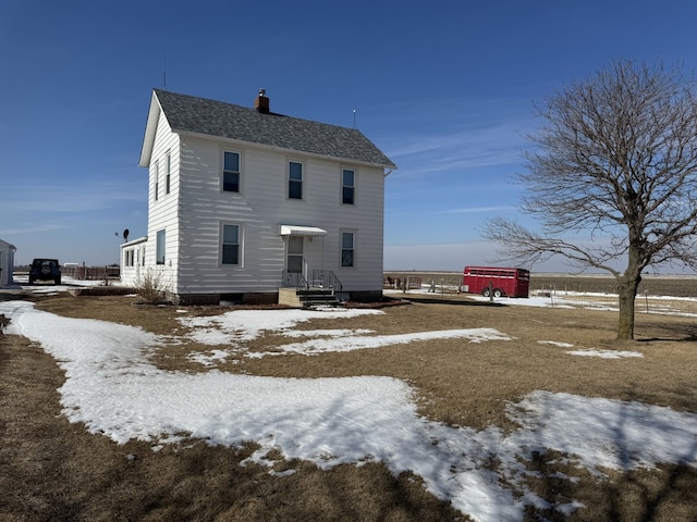 snow covered rear of property with a chimney and roof with shingles