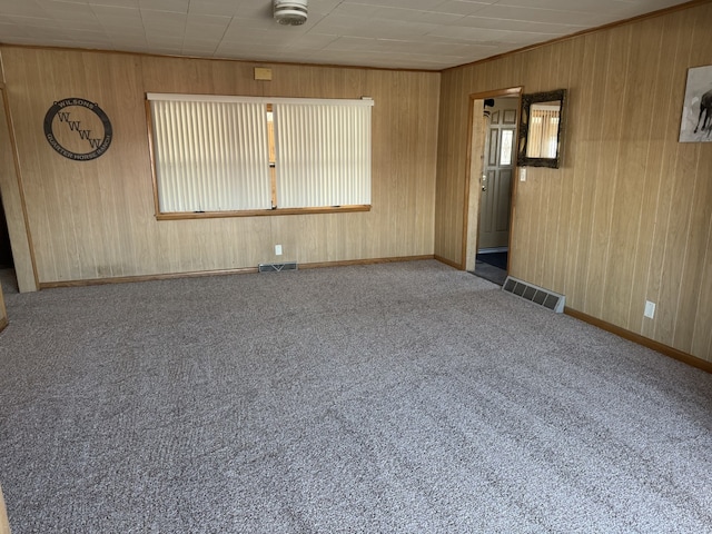 carpeted spare room with wood walls, visible vents, and baseboards