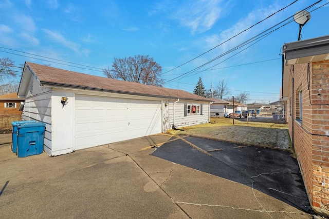 view of property exterior with a shingled roof, a detached garage, an outdoor structure, and fence