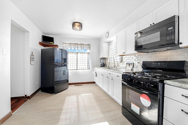 kitchen featuring baseboards, a sink, black appliances, white cabinetry, and backsplash