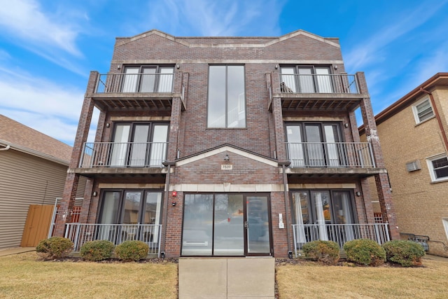 view of property featuring brick siding, a front yard, and a balcony