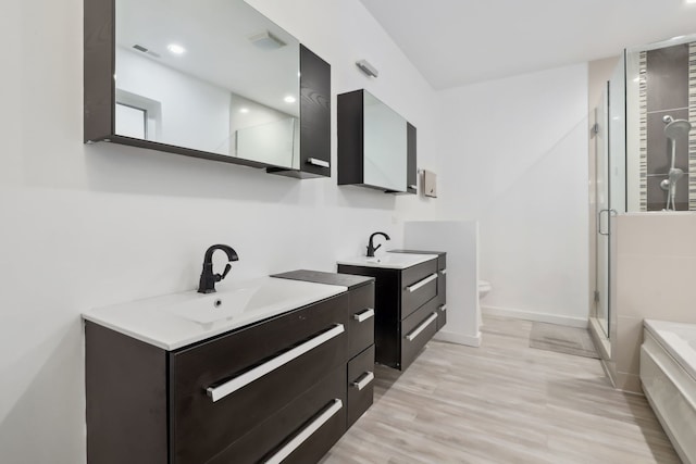 full bath with two vanities, a sink, a shower stall, and wood finished floors