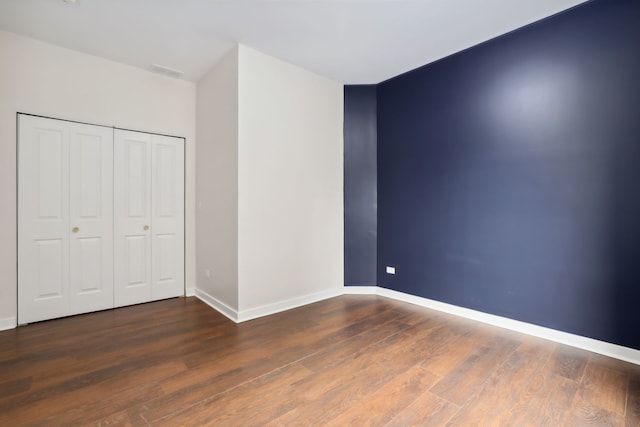 unfurnished bedroom with a closet, baseboards, and dark wood-style flooring