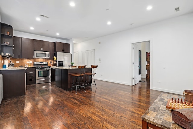 kitchen with a center island, open shelves, stainless steel appliances, visible vents, and a kitchen breakfast bar