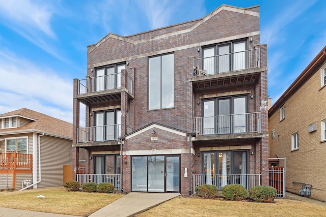 multi unit property featuring a balcony, brick siding, a front yard, and french doors