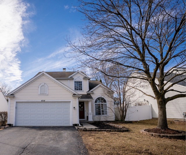 traditional-style home featuring aphalt driveway, an attached garage, and fence