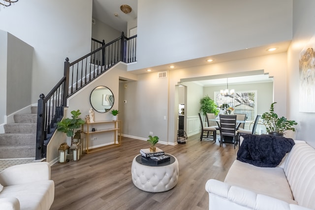 living area with visible vents, stairway, a high ceiling, wood finished floors, and a chandelier