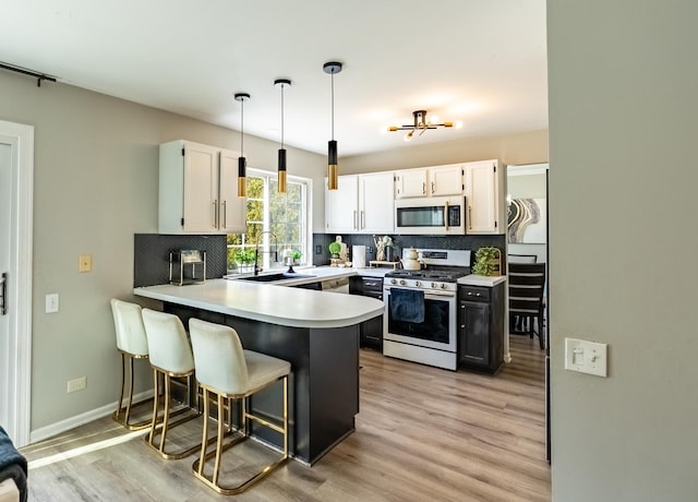 kitchen with white microwave, a peninsula, a sink, light countertops, and stainless steel gas stove