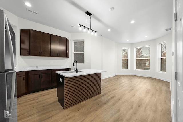 kitchen featuring decorative light fixtures, visible vents, freestanding refrigerator, a kitchen island with sink, and a sink