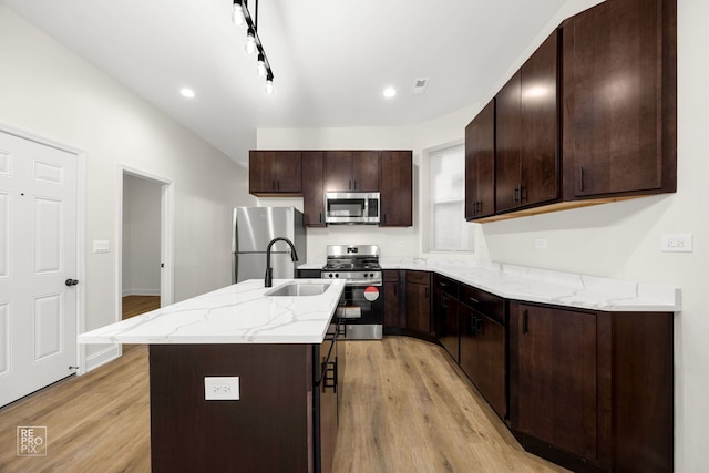 kitchen featuring stainless steel appliances, a sink, dark brown cabinets, a center island, and light wood finished floors