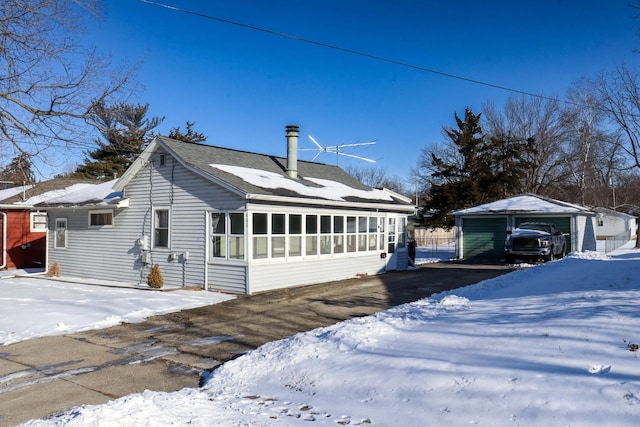 exterior space with a sunroom, a shingled roof, and an outbuilding