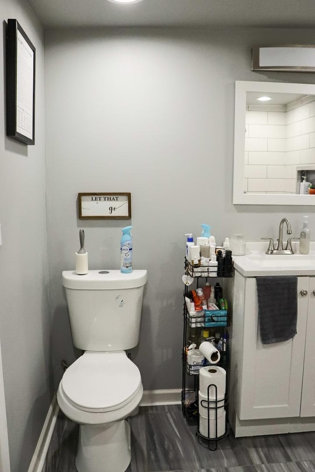 bathroom featuring baseboards, toilet, a wall unit AC, wood finished floors, and vanity